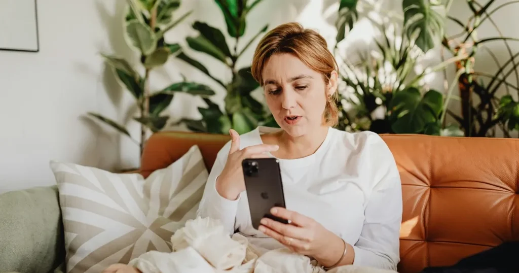 Woman reading on a smartphone while sitting on a warm leather sofa with indoor plants